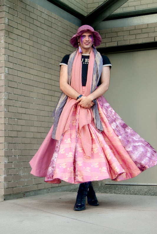 A person wearing a pink and purple floral skirt with lace panels, paired with a black top and a wide-brimmed hat.